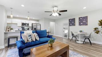 Una sala de estar moderna con un sofá azul, una mesa de centro de madera y un ventilador de techo.