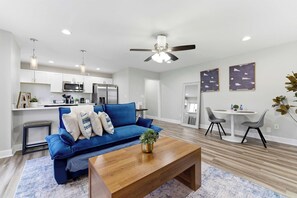Una sala de estar moderna con un sofá azul, una mesa de centro de madera y un ventilador de techo.