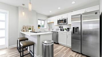 Una cocina moderna con armarios blancos, electrodomésticos de acero inoxidable y una zona de bar con taburetes.