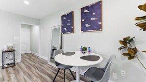 Een eetgedeelte met een ronde tafel, twee stoelen en twee abstracte schilderijen aan de muur.