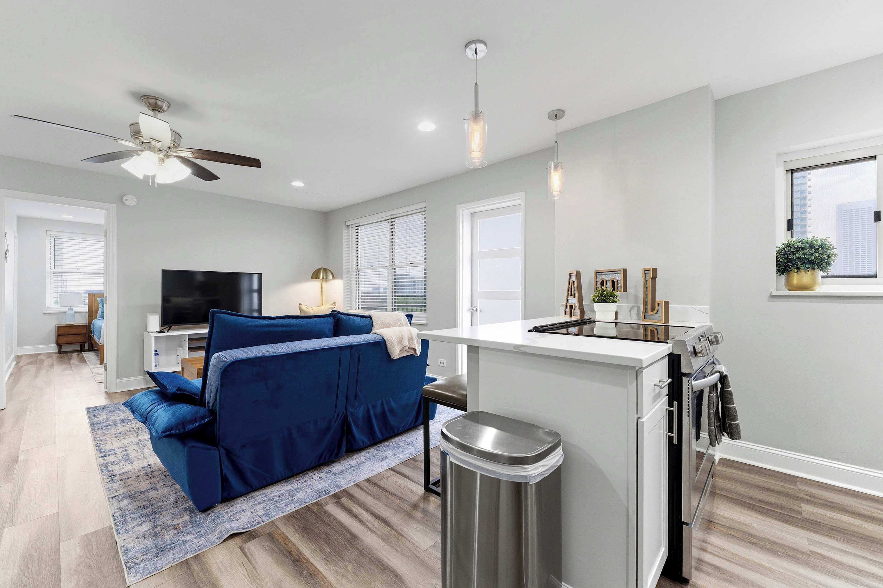 A modern apartment with a kitchenette, a ceiling fan, a flat-screen TV, and a blue sofa.