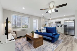 A modern living room with a sofa, coffee table, and a television. A kitchen with appliances and cabinets is visible in the background. - Cityview Peach Centrally Located (Atlanta)