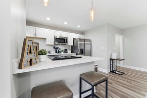 A modern kitchen with white cabinetry, stainless steel appliances, and a bar area with stools. - Cityview Peach Centrally Located (Atlanta)