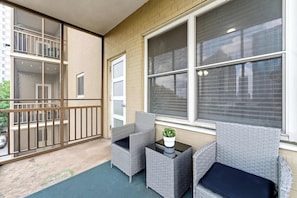 A balcony with wicker furniture, a potted plant, and a view of a building. - Cityview Peach Centrally Located (Atlanta)