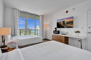 A hotel room with two beds, a TV, a desk, and a window with a city view. - Condo Resort - Beach access & Bay View (Hallandale Beach)
