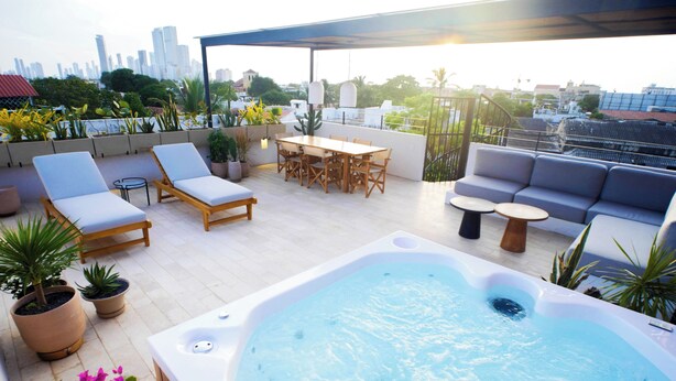 Una terraza en la azotea con jacuzzi, sillones de descanso, una mesa de comedor y un sofá.