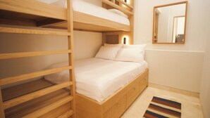 Una cama litera con estructura de madera y ropa blanca, una mesita de noche pequeña y un espejo en la pared.