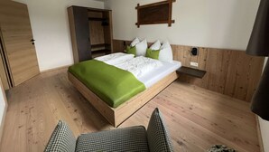 A bedroom with a bed, a wooden wardrobe, a small bedside table, and a wall-mounted shelf. - Studler-Eck - Holidays at the most beautiful place in the Tyrol (Oberperfuss)