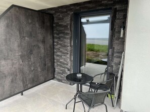 A modern outdoor seating area with a glass door leading to a patio, featuring a stone wall and a view of the outdoors. - Studler-Eck - Holidays at the most beautiful place in the Tyrol (Oberperfuss)