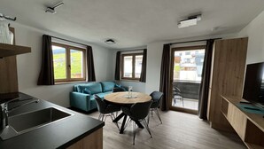 Une cuisine moderne équipée d’un évier, un coin repas avec une table ronde et des chaises, un canapé et de grandes fenêtres avec des rideaux.