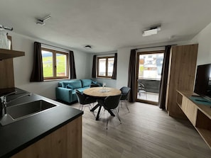 Eine moderne Küche mit Spüle, ein Essbereich mit rundem Tisch und Stühlen, eine Couch und große Fenster mit Vorhängen.