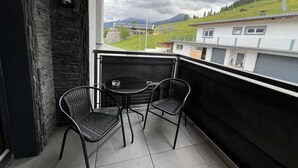 Un balcon avec deux chaises et une table, donnant sur un paysage verdoyant parsemé de bâtiments.