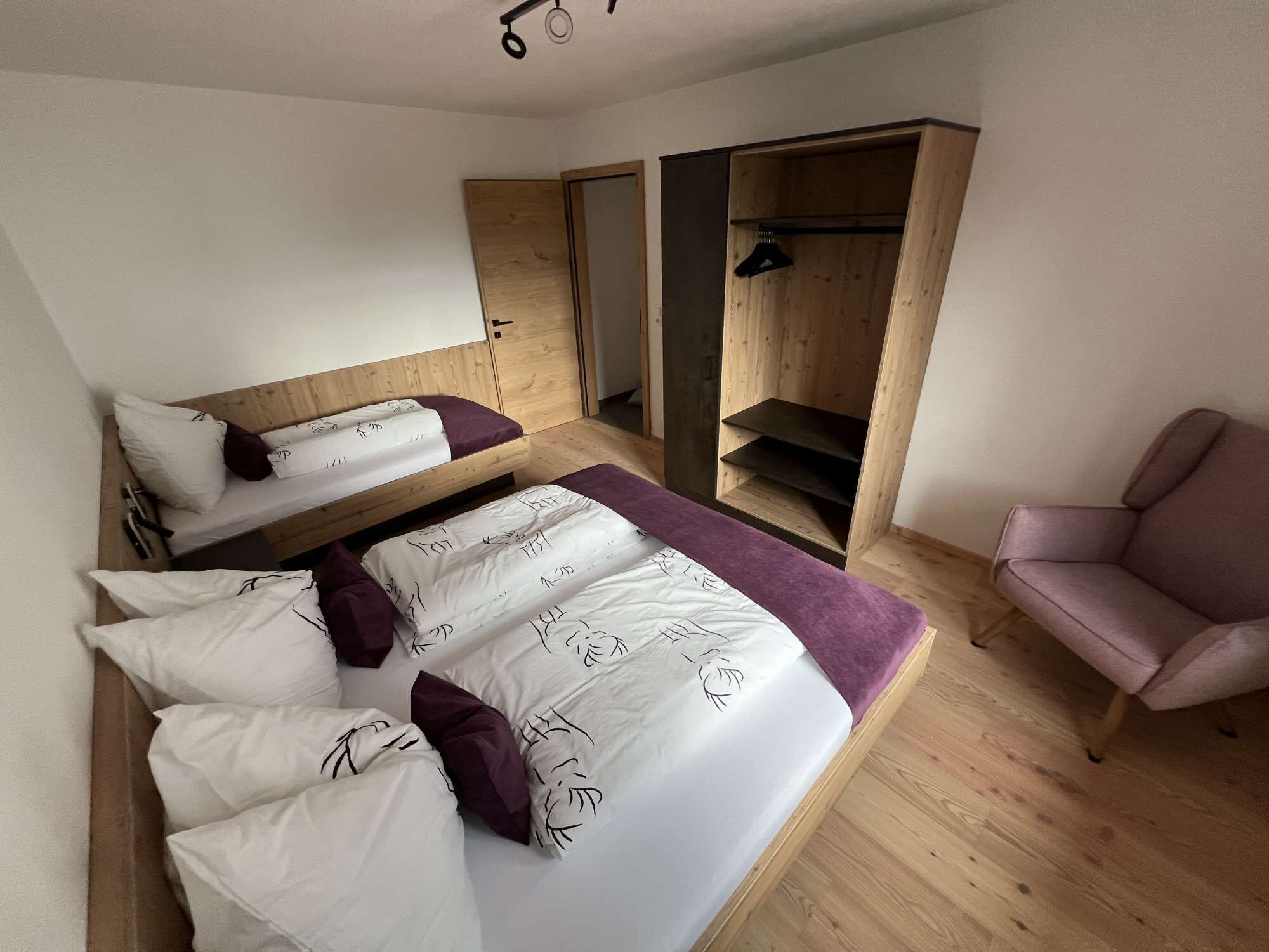 Une chambre moderne avec un lit superposé, un lit simple, une chaise et des étagères en bois intégrées.