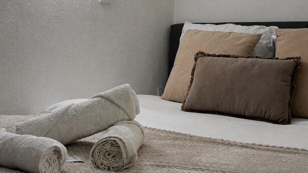 A minimalist hotel room with a bed, a textured rug, and a wall-mounted light fixture. - Le Nid Vaillant - Near the Train Station & Free Parking (Tours)