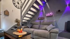 A modern living room with a grey sofa, a wooden coffee table with candles, a clock, and a neon 'love' sign on the wall. - Le Nid Vaillant - Near the Train Station & Free Parking (Tours)
