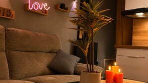 A modern living room with a sofa, a coffee table, a potted plant, candles, and a neon sign on the wall. - Le Nid Vaillant - Near the Train Station & Free Parking (Tours)