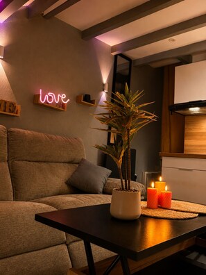 Uma sala de estar moderna com sofá, mesa de centro, planta em vaso, velas e um letreiro de neon na parede.