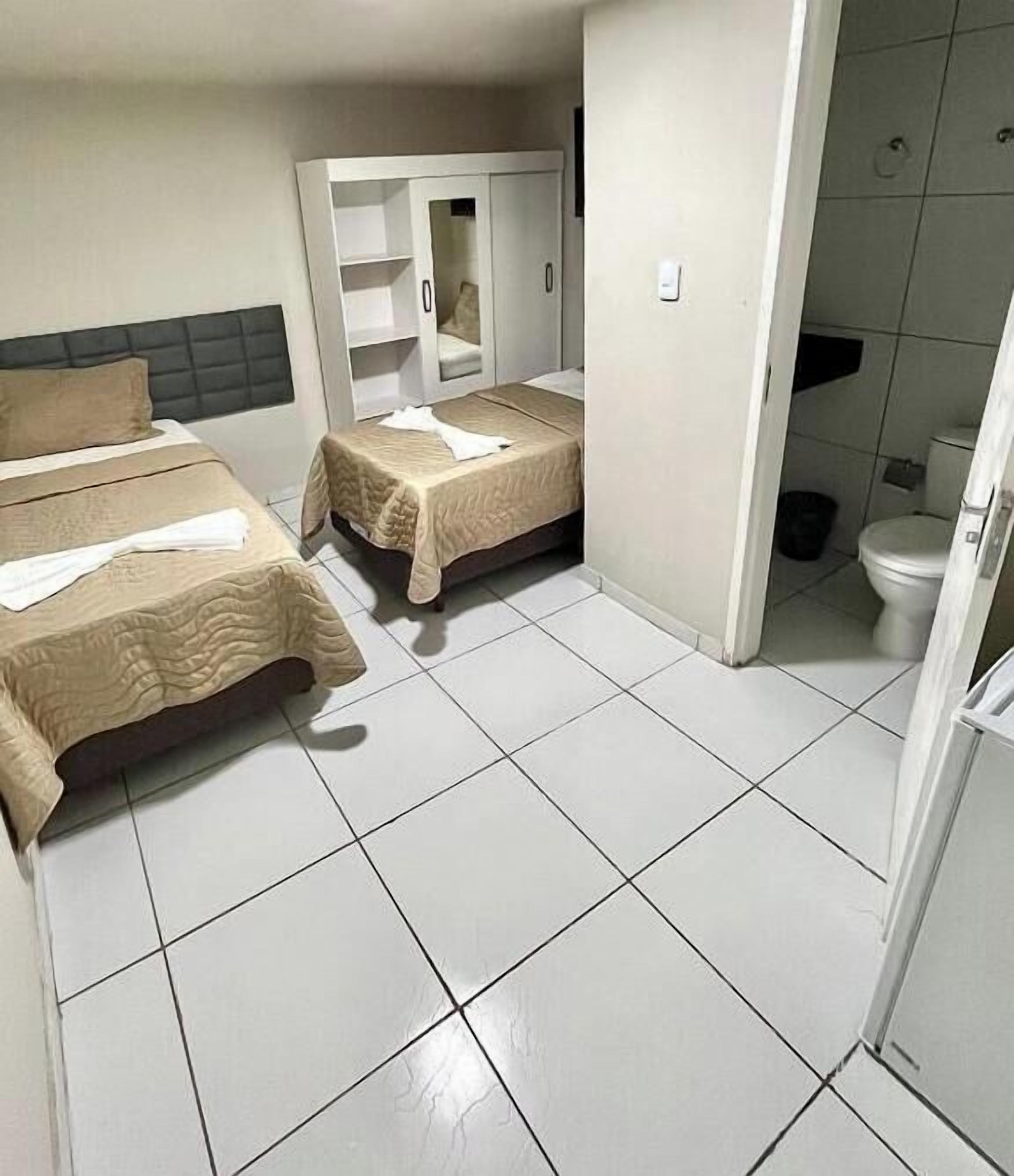A hotel room with two beds, a wardrobe, and a bathroom.