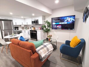 Un salon moderne comprenant un canapé, un fauteuil, une table basse et un téléviseur à écran plat fixé au mur.
