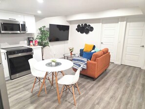 A modern kitchen with a microwave, stove, and dining area with chairs and a table. - Cozy 2 Bedroom Legal Suite/Sleeps 4 (Edmonton)