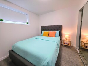 A bedroom with a bed, a window with a plant, and bedside lamps. - Cozy 2 Bedroom Legal Suite/Sleeps 4 (Edmonton)