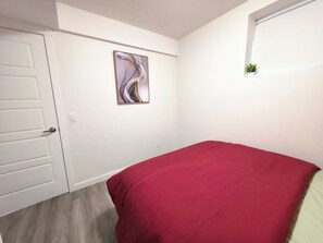 A bedroom with a bed, a door, a wall-mounted picture, and a small window. - Cozy 2 Bedroom Legal Suite/Sleeps 4 (Edmonton)