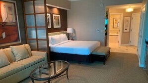 Ein Hotelzimmer mit einem Bett, einem Schlafsofa, einem Glastisch und einer Tür zu einem Flur.