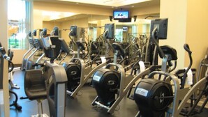 Ein Fitnessstudio mit verschiedenen Cardiogeräten, Spiegeln und einem Bildschirm.