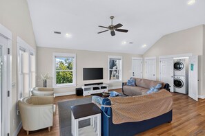 A spacious living room with a large sofa, a television, and a ceiling fan. - Waterfront & Sunset Views!!  3-bedroom house on Albemarle Sound (Kill Devil Hills)