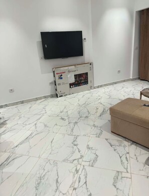 Um quarto com uma TV montada, uma caixa com a inscrição 'SHARP 55 4K Ultra HD TV' e piso com padrão marmorizado.