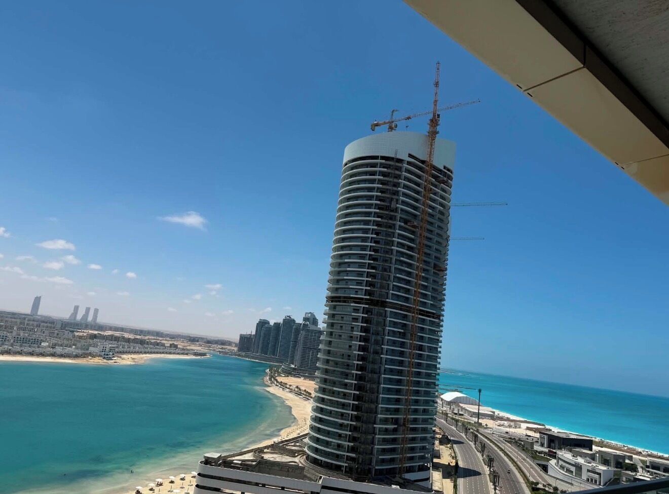 Ein Hochhaus mit einem Baukran, einem Strand und einem wolkenlosen, blauen Himmel.