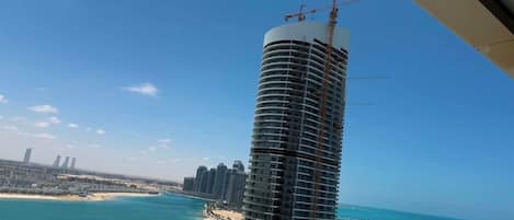 A high-rise building with a construction crane, a beach, and a clear blue sky.