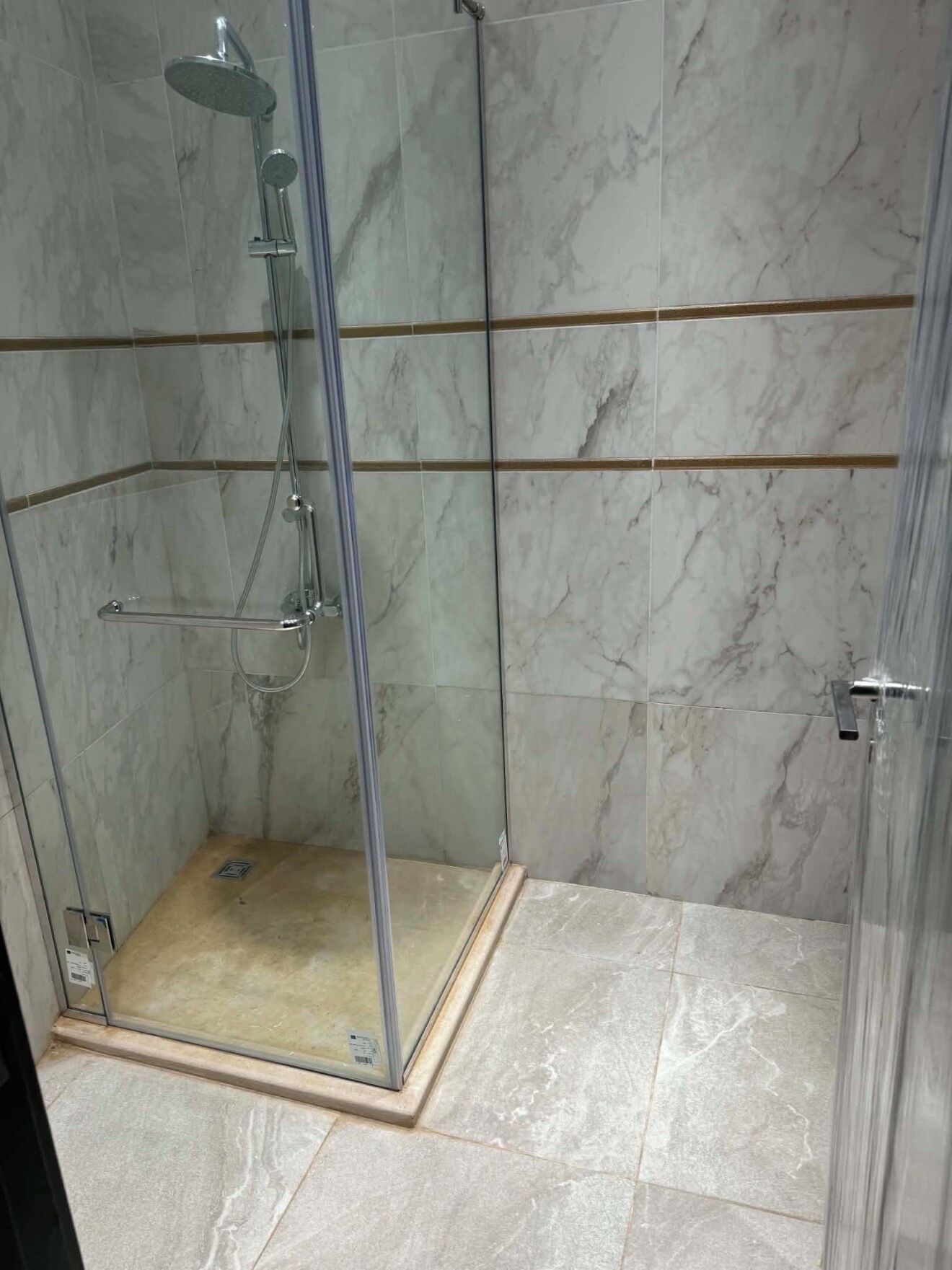 A glass-enclosed shower stall with a handheld showerhead and a wall-mounted faucet.