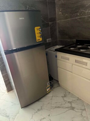 Uma cozinha com geladeira de aço inoxidável, fogão e lixeira.