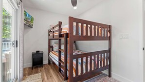 Ein Stockbett mit Holzbettrahmen und gestreifter Bettwäsche, ein kleiner Nachttisch und Blick ins Freie durch eine Schiebetür.