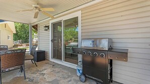 Eine Terrassengrundstück mit Holzkohlegrill, einer Glastür zu einem überdachten Bereich und einem Metalltisch mit Stühlen.