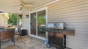 Eine Terrassengrundstück mit Holzkohlegrill, einer Glastür zu einem überdachten Bereich und einem Metalltisch mit Stühlen.