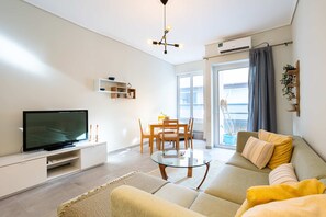 A modern living room with a flat-screen TV, a glass coffee table, a sofa, and a dining area with a table and chairs. - Seaside Retreat for Relaxed Kalamata Beach Stays (Kalamata)