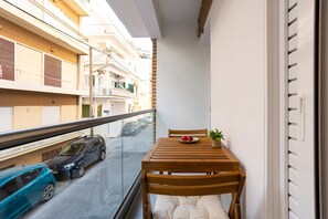 A balcony with a wooden table, a chair, a potted plant, and a bowl of fruit. - Seaside Retreat for Relaxed Kalamata Beach Stays (Kalamata)