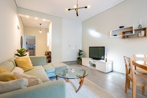 A modern living room with a sofa, a glass coffee table, a TV, and a dining area. - Seaside Retreat for Relaxed Kalamata Beach Stays (Kalamata)