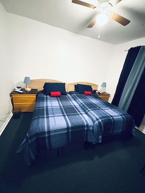A bedroom with a bed, two bedside tables, a ceiling fan, and a window with curtains.