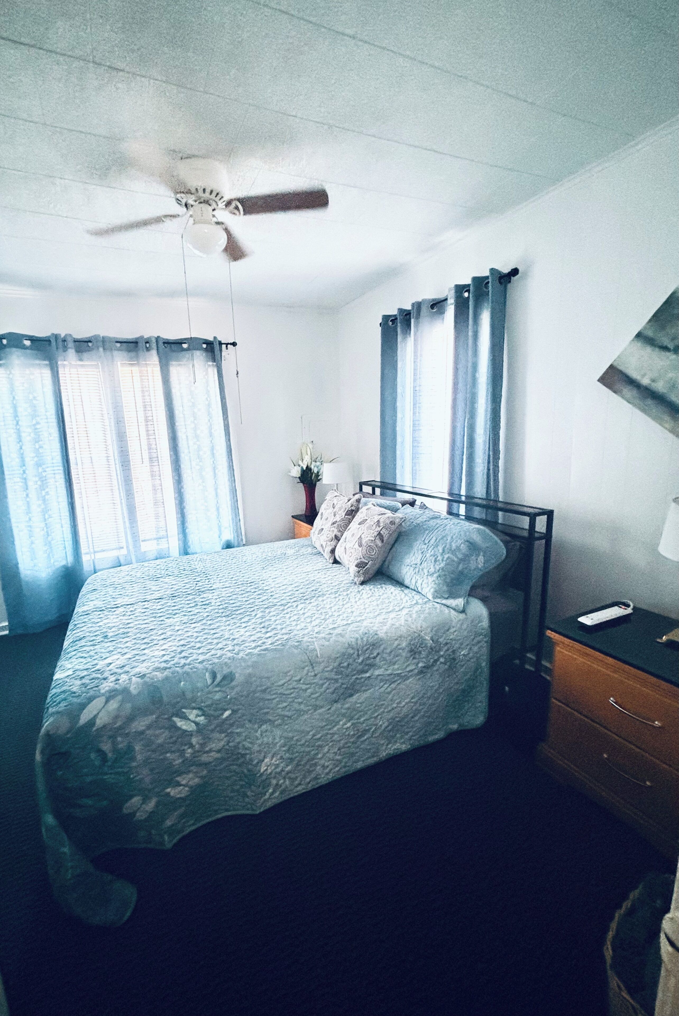 A bedroom with a bed, a nightstand, a lamp, curtains, and a ceiling fan.