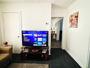 A living room with a flat-screen TV on a wooden stand, a sofa, and a hallway leading to another room.