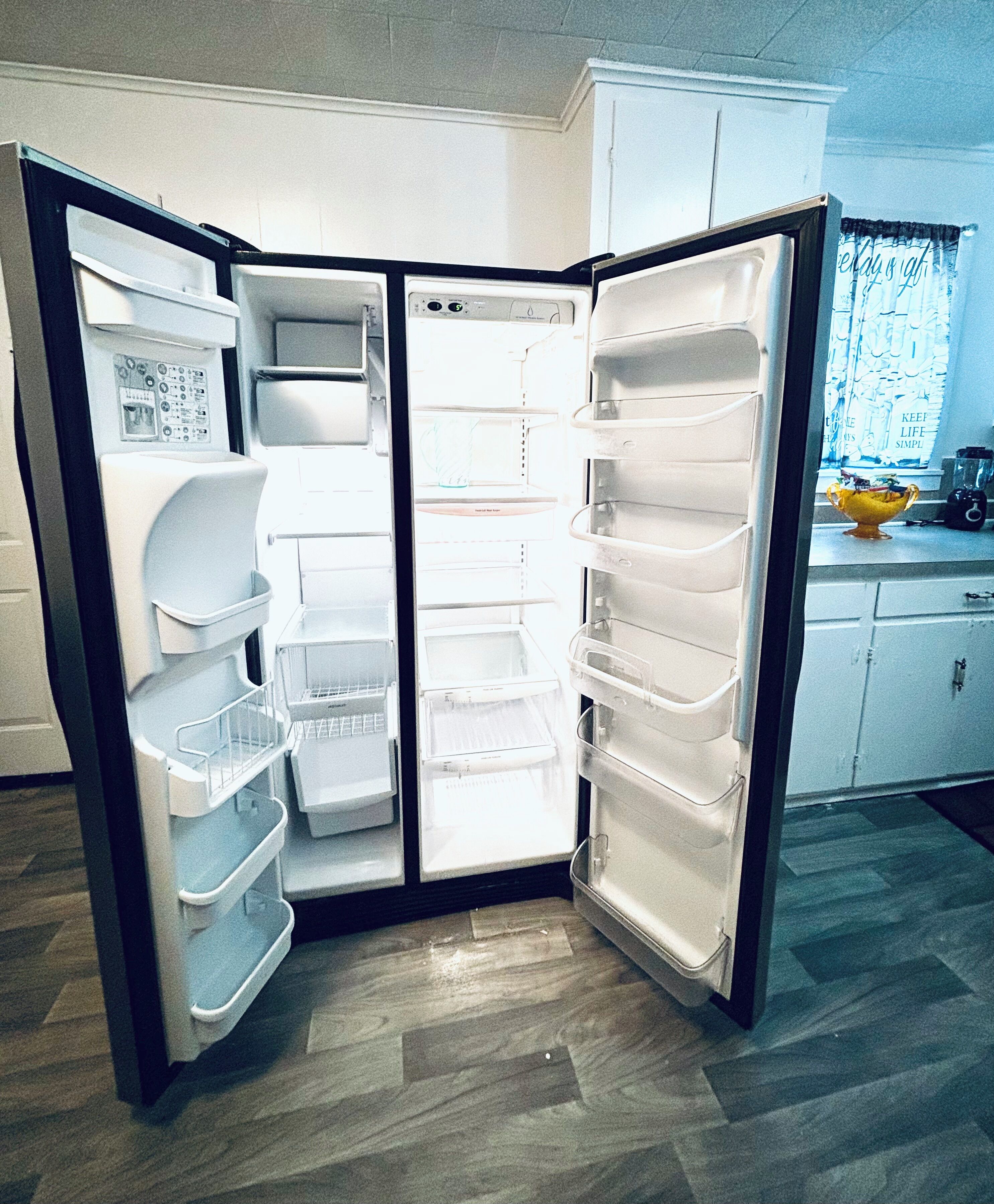 A compact refrigerator with multiple shelves and compartments, situated in a kitchen with wooden flooring and white cabinetry.