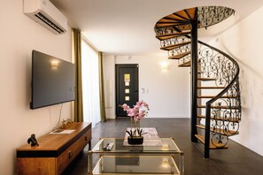 Ein modernes Interieur mit einem Flachbildfernseher, einem Glastisch mit Blumenvase, einer Holzkonsole und einer Wendeltreppe.