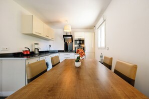 A modern kitchen with white cabinets, a wooden dining table, and a vase with flowers. - Saphir 6 Apartment (Cannes)