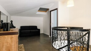 En modern inredning med en svart soffa, ett träskåp och en trappa med utsmyckade metallräcken.