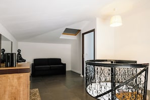 A modern interior with a black sofa, a wooden cabinet, and a staircase with ornate metal railings. - Saphir 6 Apartment (Cannes)