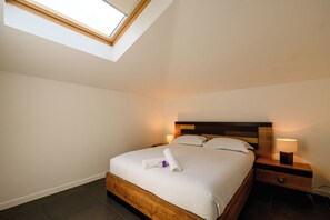 Een hotelkamer met een dakraam, een houten bedframe, een nachtkastje en een bedlamp.