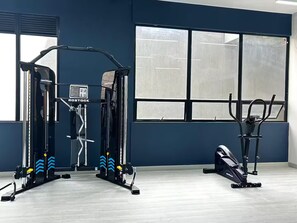 Un gimnasio con equipo de ejercicio, ventanas amplias y una pared azul.